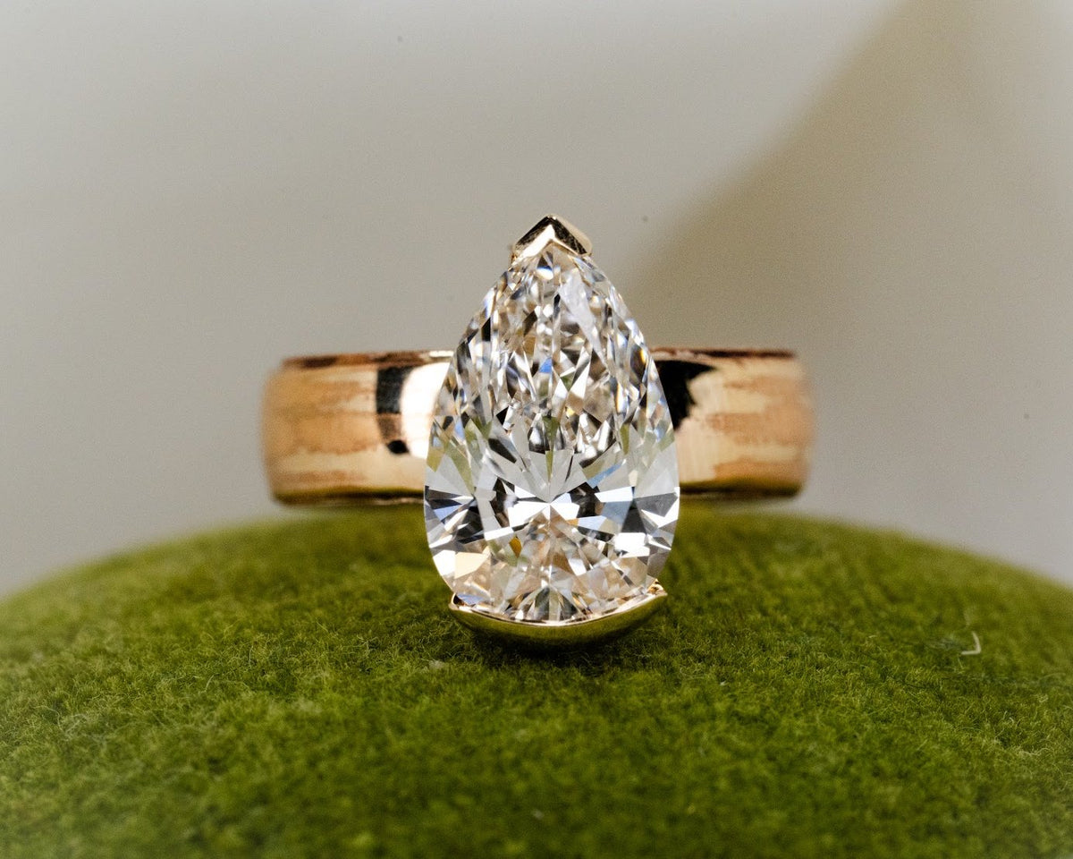 Pear-shaped diamond engagement ring with a wide yellow gold band